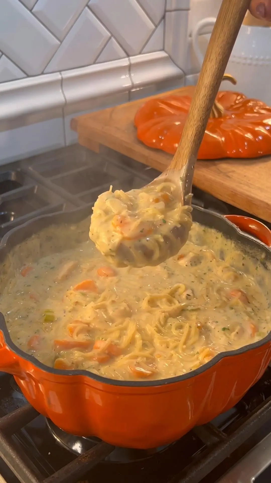 Wooden spoon lifting creamy chicken noodle soup with noodles and vegetables from a pot