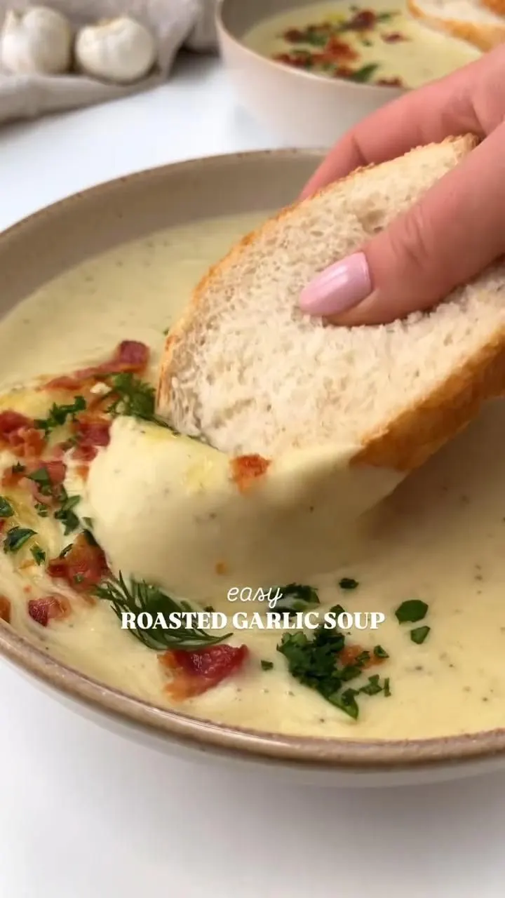 Bowl of creamy roasted garlic soup topped with croutons, bacon bits, and fresh parsley