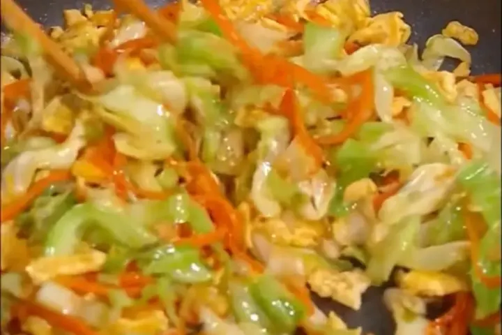 Vegetable stir-fry with cabbage, carrots, and scallions in a wok with savory sauce