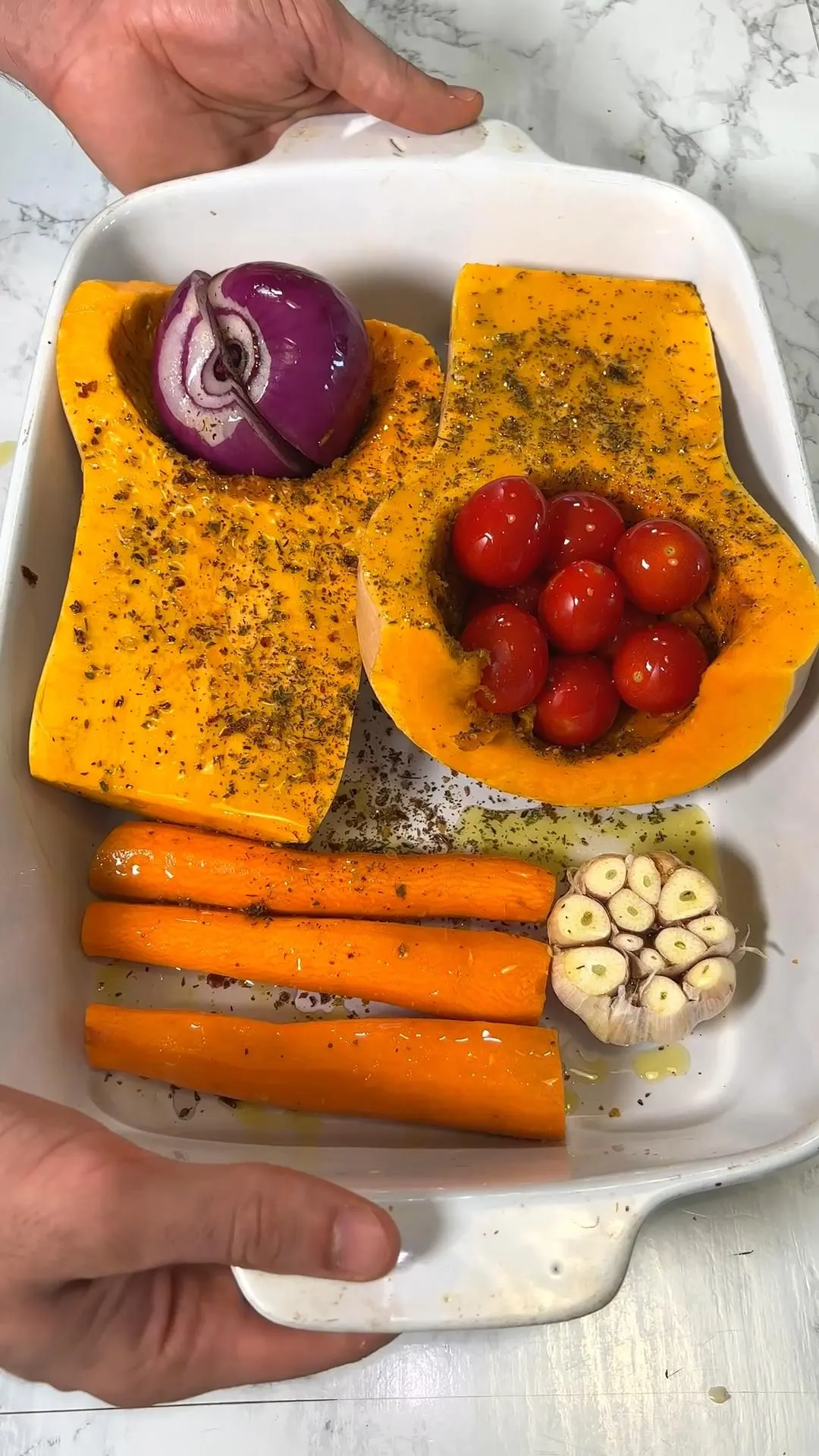 Raw butternut squash, carrots, cherry tomatoes, red onion, and garlic seasoned in a baking dish before roasting for soup